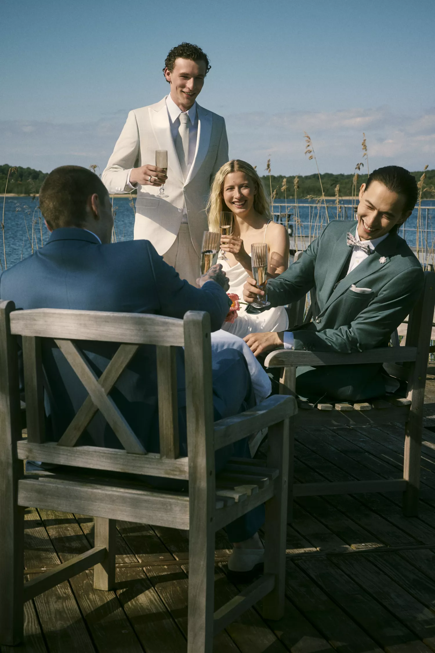 Elegante Gesellschaft in Anzügen stößt bei Sonnenschein am Steg mit Sekt an